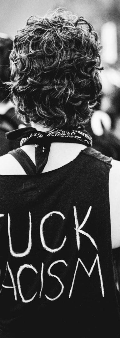 A person seen from behind, in black and white. Their shirt reads "Fuck Racism."
